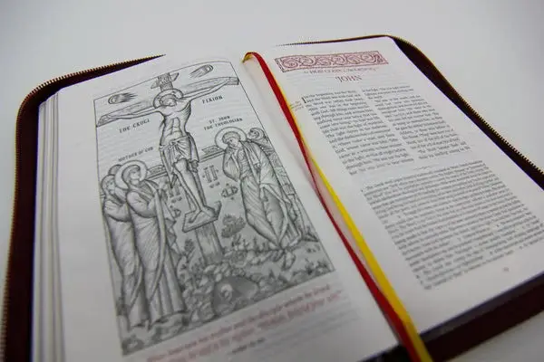 The Eastern Orthodox Bible New Testament lying open to an engraving of the crucifixion, with red and gold ribbon markers