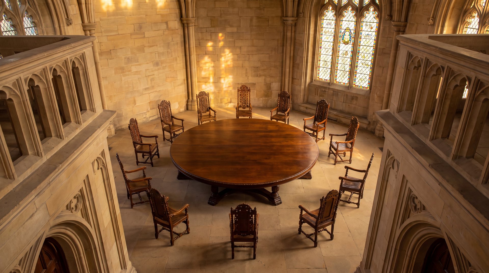 The round table of the Order of the Lamplighters: twelve carved chairs around an oak table, with a lit brass lamp before each chair